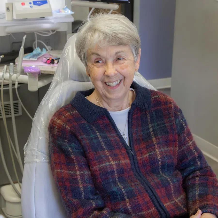 Smiling elderly woman sitting in a dental chair during a friendly dental consultation.