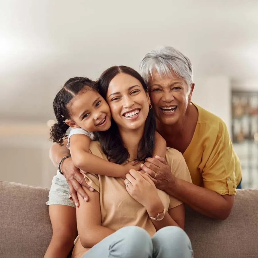 Three generations of women smiling together, showcasing love and connection in a cozy living room setting.