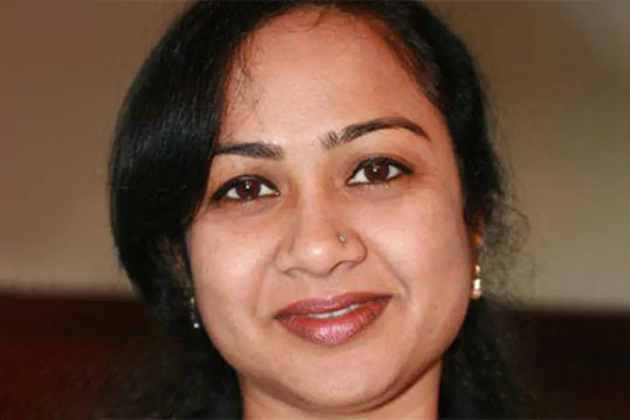 Close-up portrait of a smiling woman with dark hair and a nose piercing against a neutral background