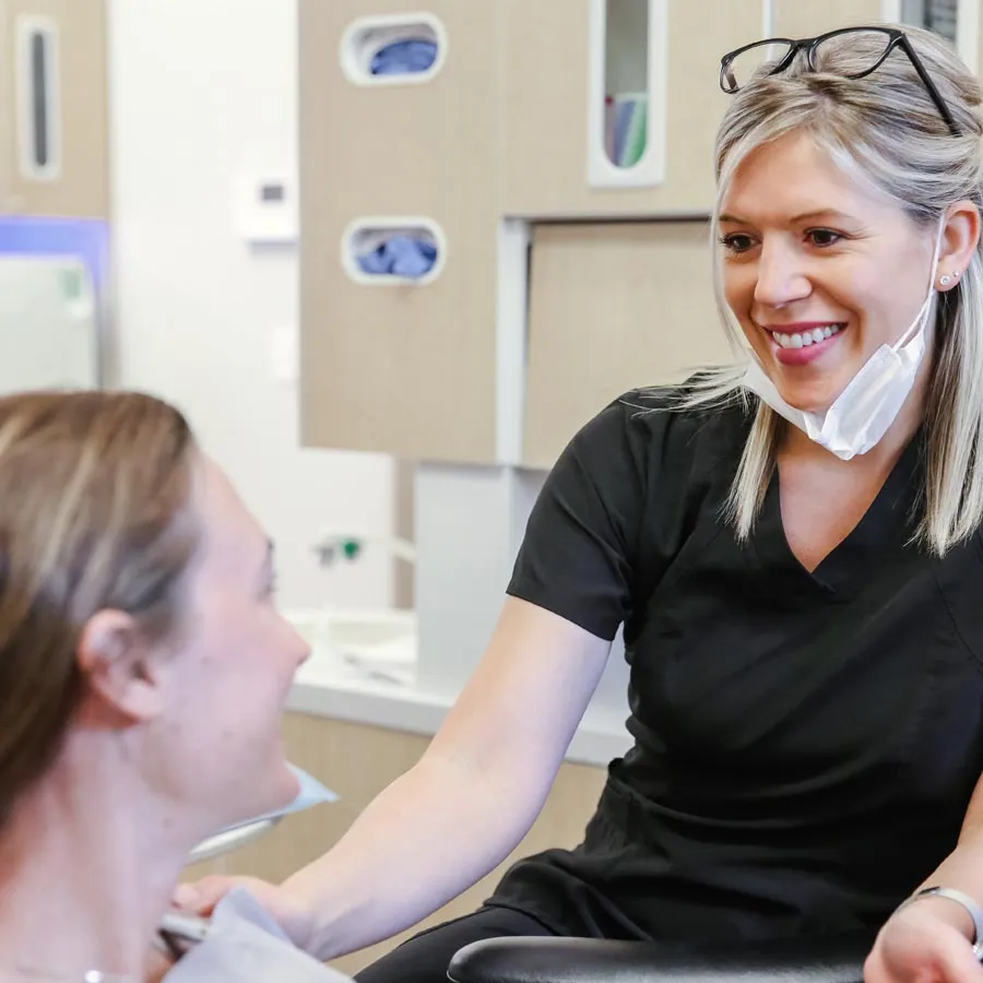 A dental professional smiles at a patient in a modern clinic setting during a consultation.