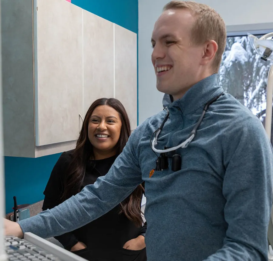 Male dentist and female patient smiling in dental clinic with computer and equipment in background