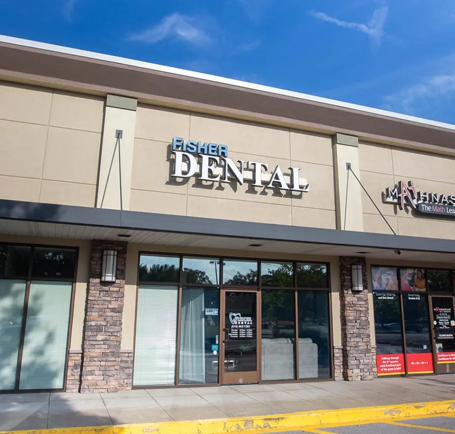 Storefront of Fisher Dental with large signage on beige building under blue sky in a shopping plaza.