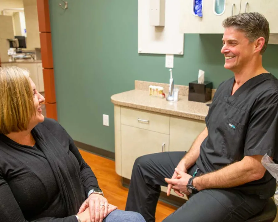 Smiling female patient and male healthcare professional in black scrubs talking in a medical office with green walls.