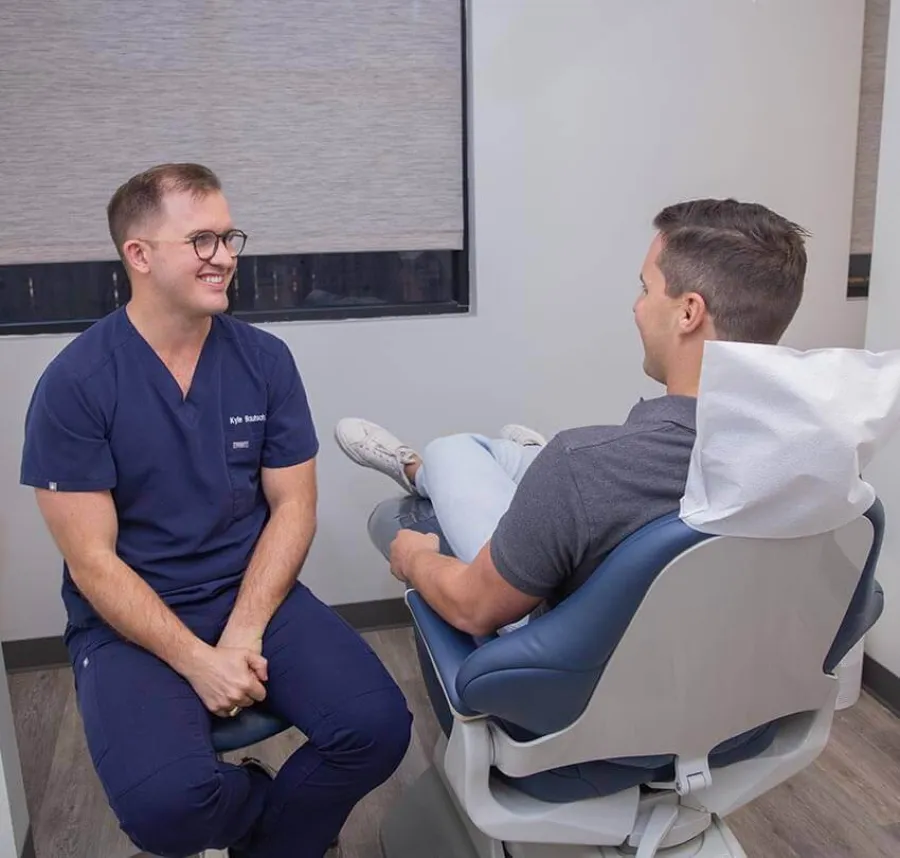 Smiling male dentist consulting with patient seated in dental chair in a modern clinic room.