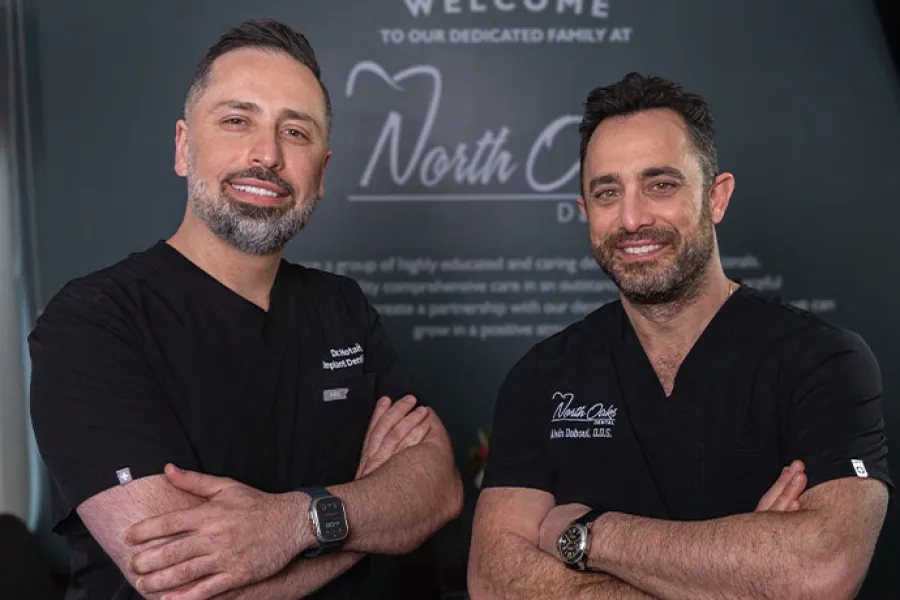 Two smiling male dentists with crossed arms in black scrubs standing in front of a North City Dental sign.
