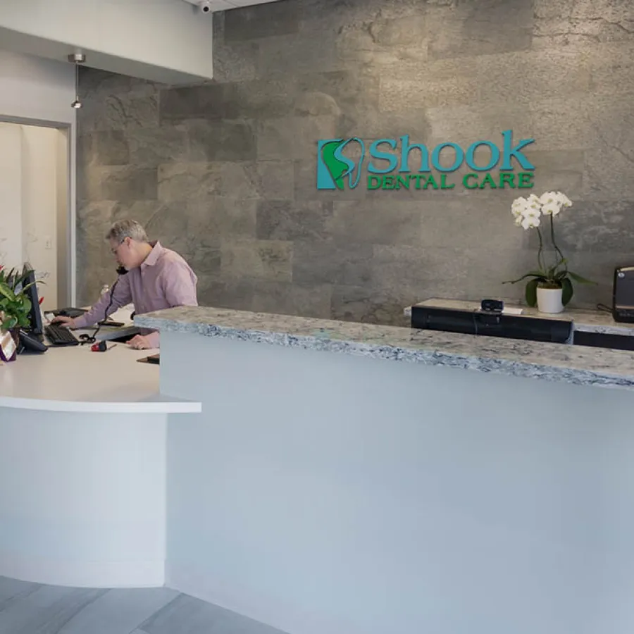 Reception area of Shook Dental Care with a receptionist on the phone and a stone wall with logo.