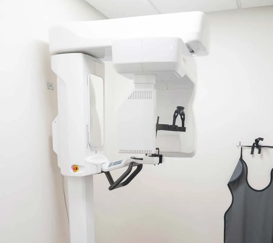 Modern dental panoramic X-ray machine in a clean, white dental clinic room with protective lead apron visible