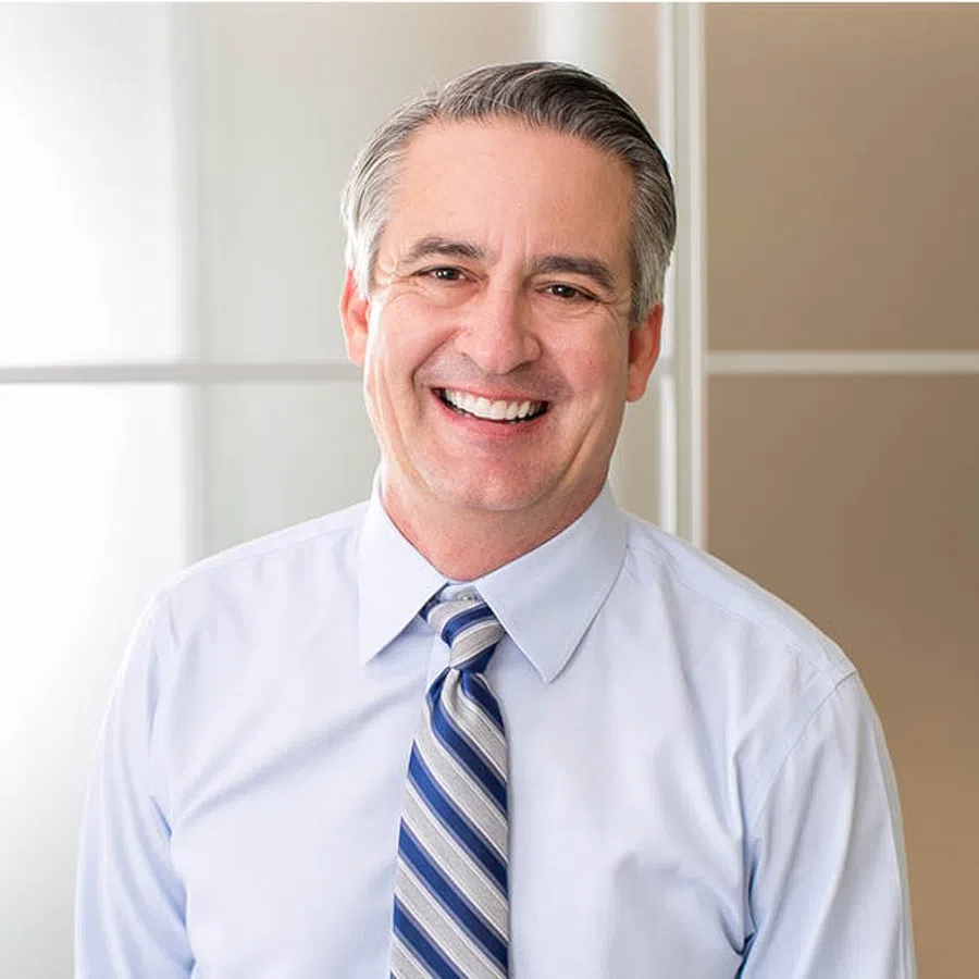 Smiling middle-aged man in a light blue shirt and striped tie standing in a bright modern office.