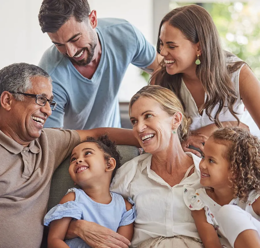 Happy multigenerational family smiling and enjoying time together indoors on a couch in natural light