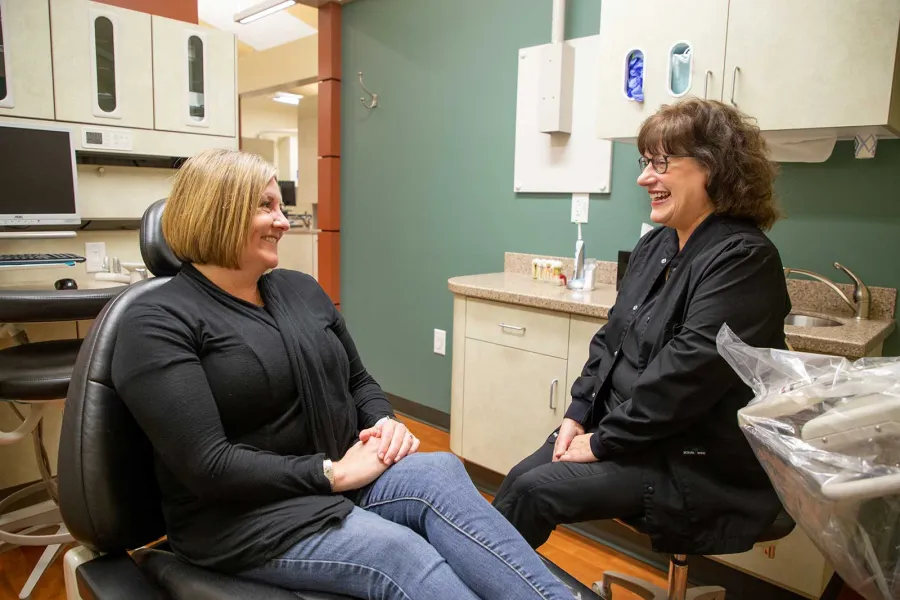Patient and dental professional smiling and conversing in a modern dental office consultation room.