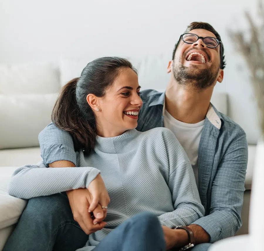 Happy couple sitting close together laughing and holding hands in a cozy living room setting.