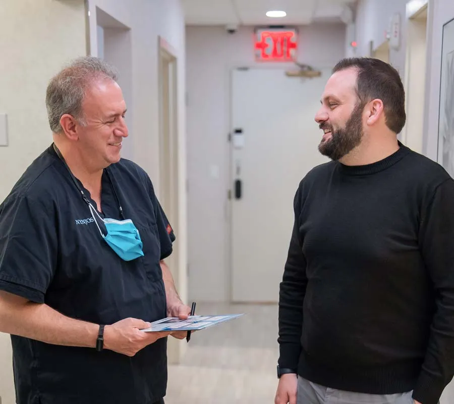 Doctor in scrubs and a patient smiling and talking in a medical clinic hallway with exit sign.