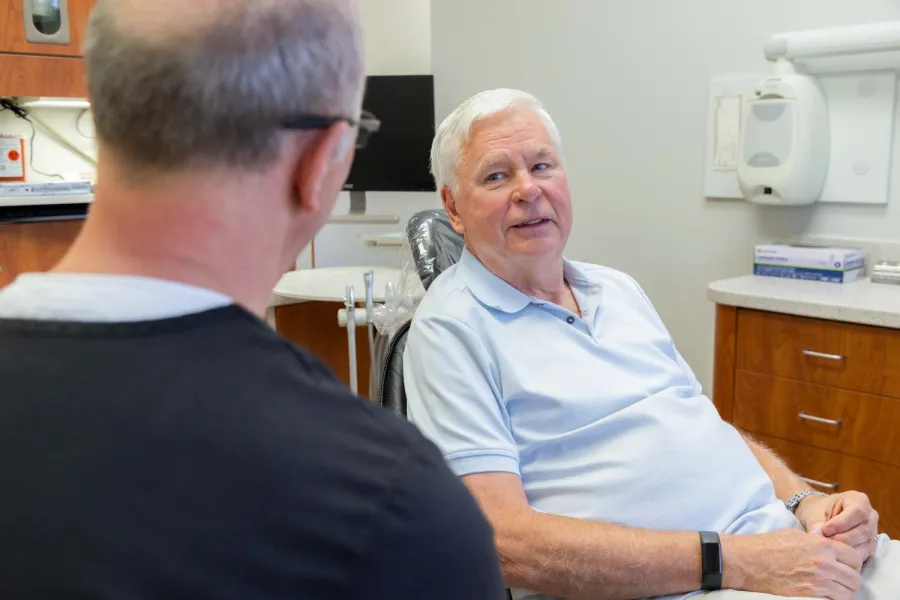 Senior man in light blue shirt consulting with dentist in a modern dental office setting.