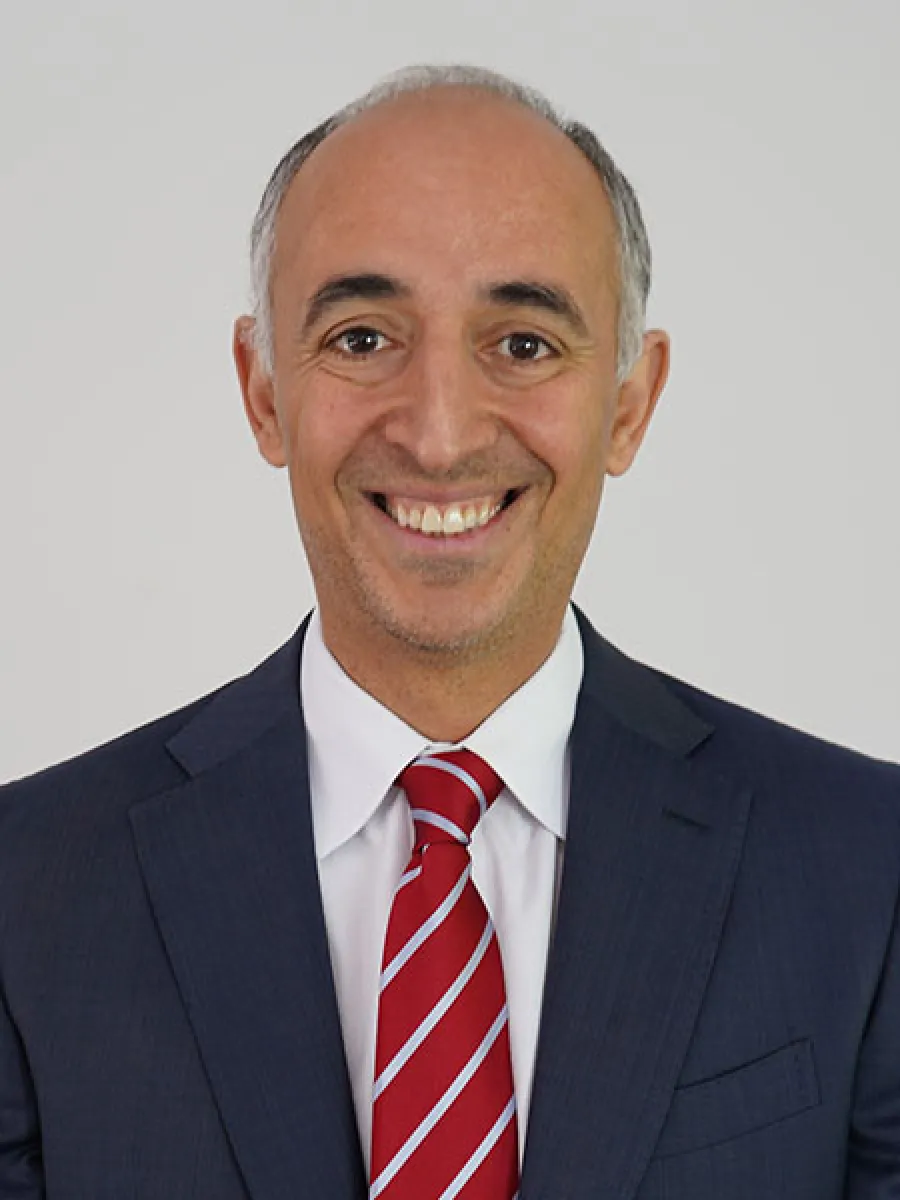 Smiling man in a suit and tie presenting a professional appearance against a plain background.
