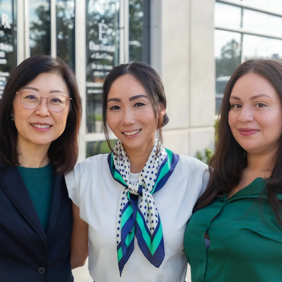 Three diverse women smiling outdoors in front of a building, showing friendship and professional attire.