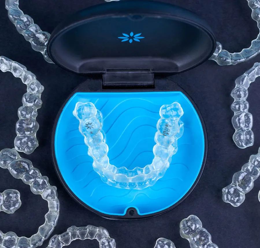 Clear dental aligners arranged around a black and blue storage case on a dark surface.