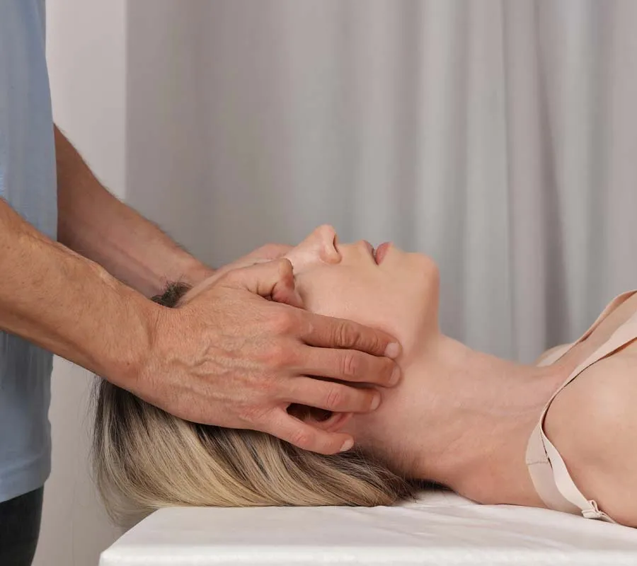 Therapist performing gentle neck and head massage on a woman lying down with closed eyes.