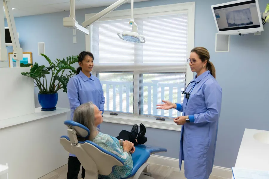 Dentist and assistant discussing treatment with patient in modern dental office with blue decor.
