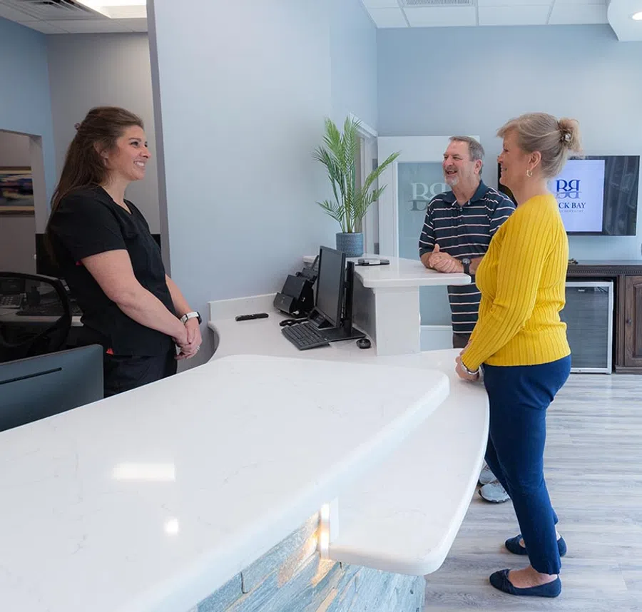 Receptionist at Back Bay Family Dentistry smiles to a man and a woman