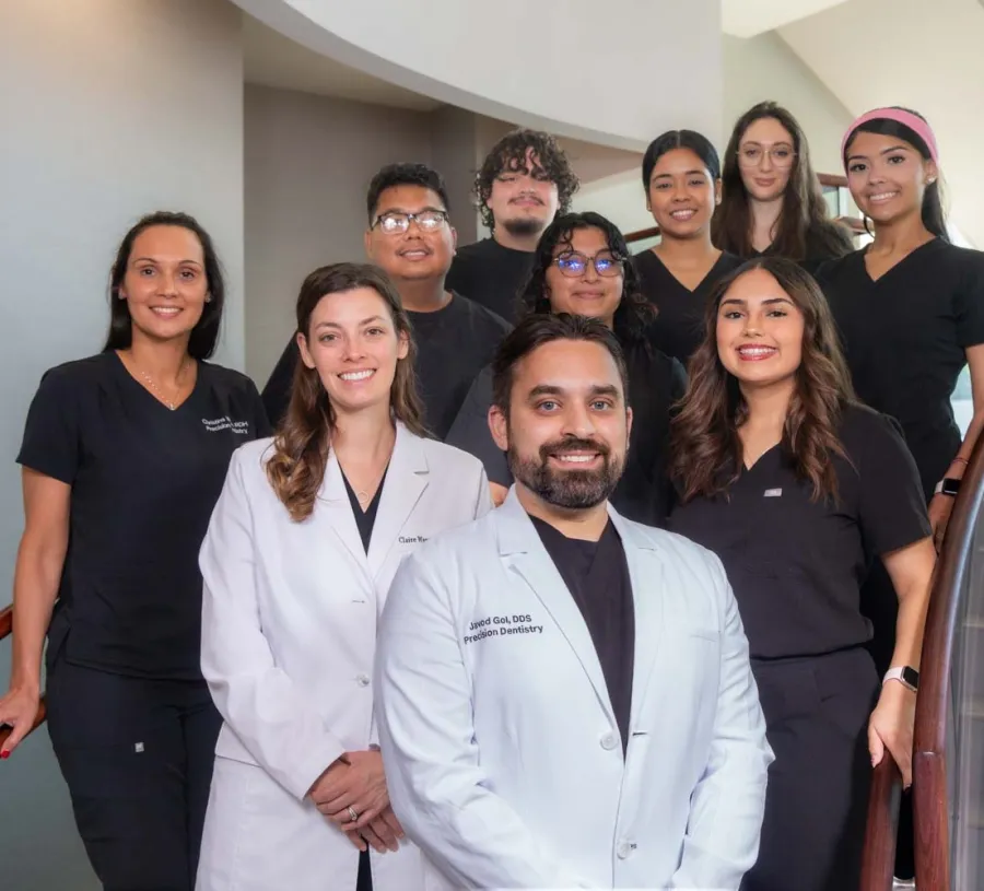 Group portrait of smiling dental team members in professional attire standing on a staircase inside a clinic