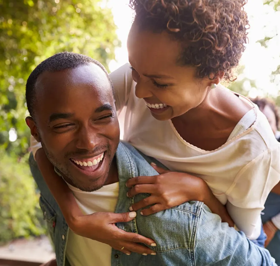 Happy couple laughing together outdoors with woman piggybacking on man in casual clothing.