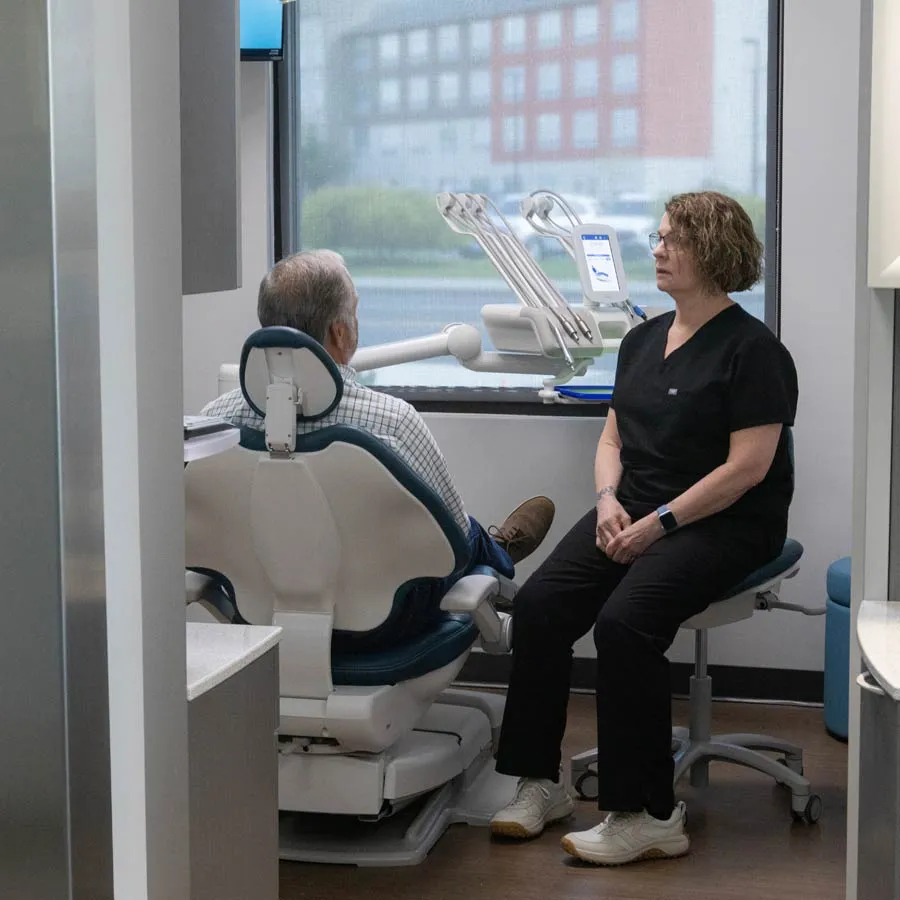 Dentist in black scrubs consulting with a seated male patient in a modern dental clinic with equipment.