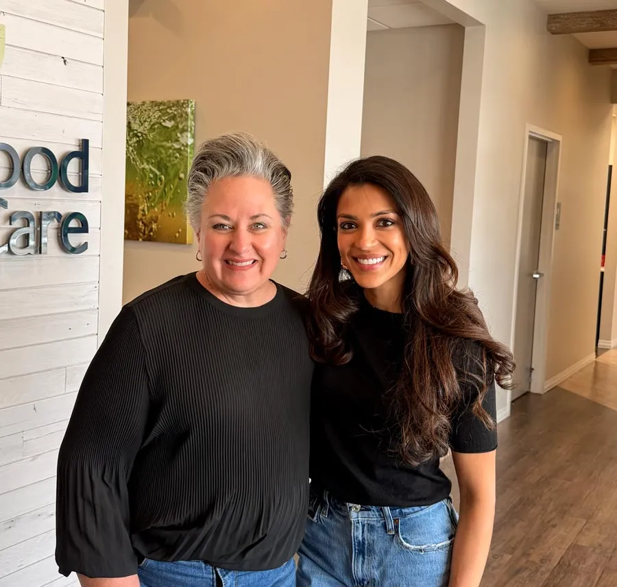 Two women smiling in a modern office hallway with natural light and casual attire.