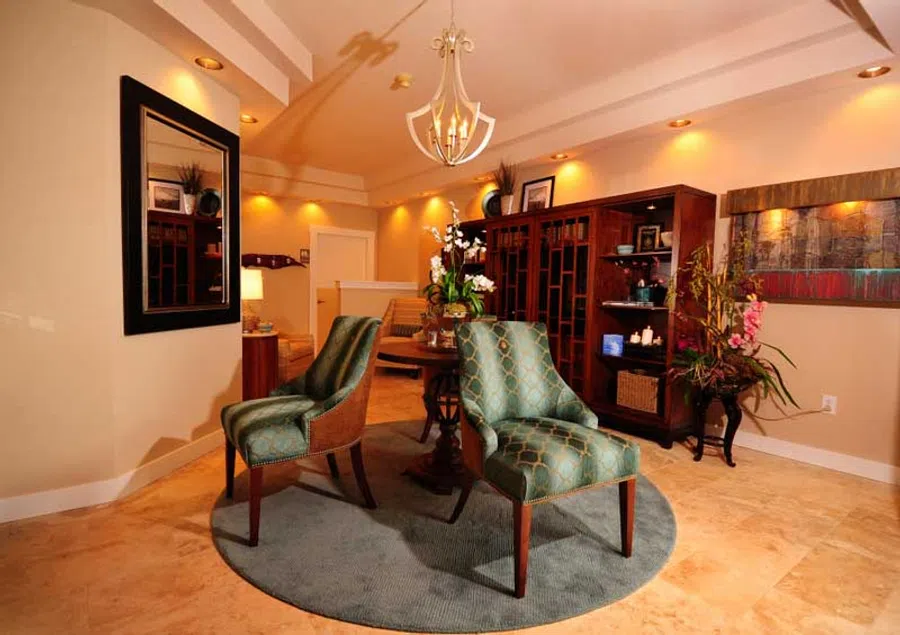 Elegant living room with teal patterned chairs, round rug, wooden cabinet, chandelier, and warm lighting.