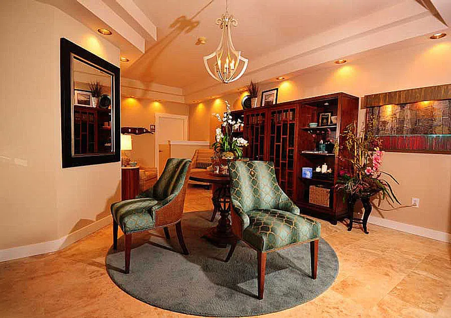 Cozy sitting area with two patterned chairs on round rug, wooden cabinet, flowers, and warm lighting in living room