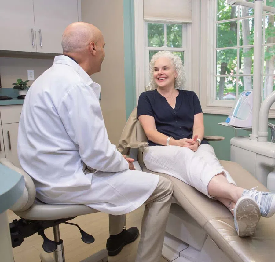 Doctor in white coat consulting with smiling female patient seated in a dental office chair.