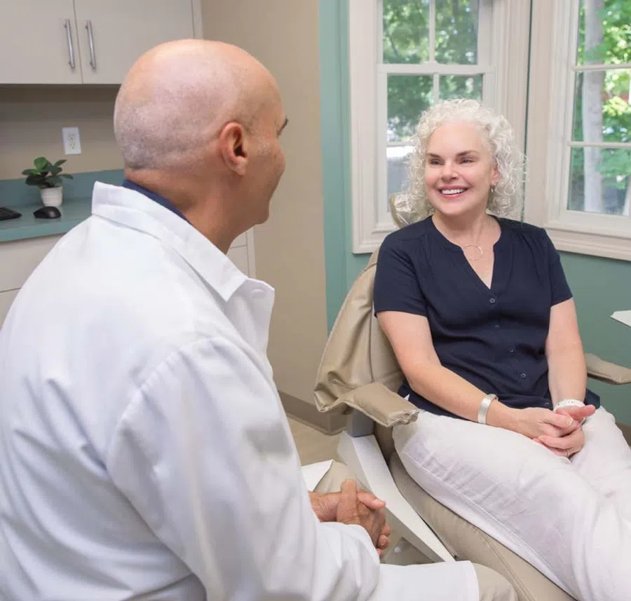 Smiling elderly woman seated in a medical office talking with a doctor in white coat during consultation.