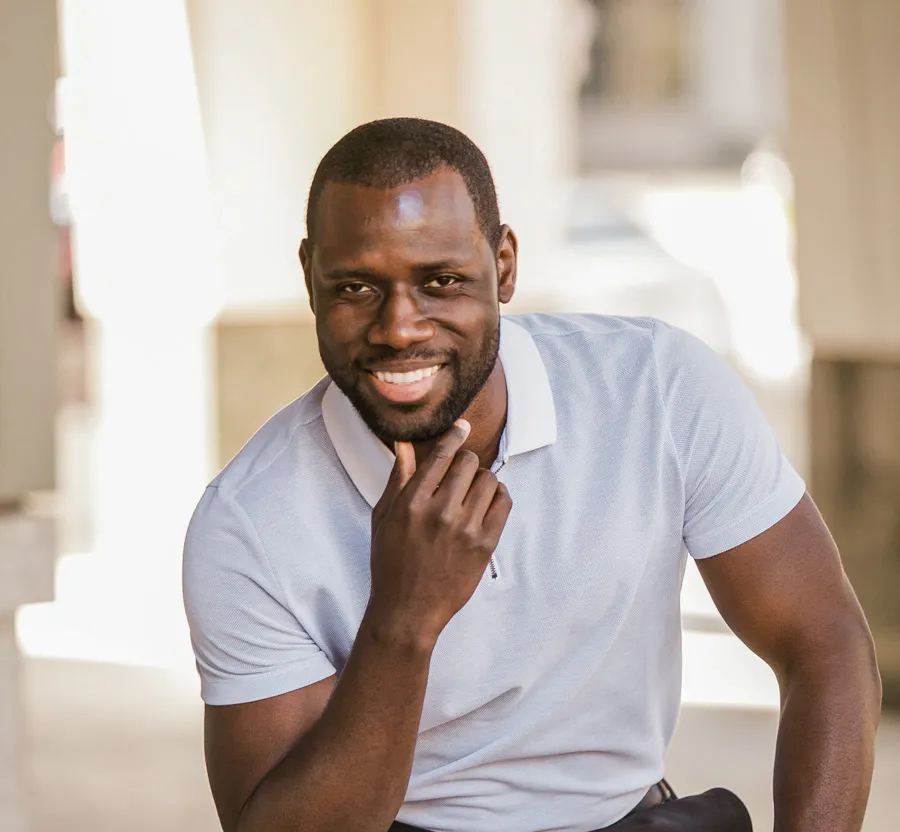 Smiling man in white polo shirt posing with hand on chin in bright indoor setting