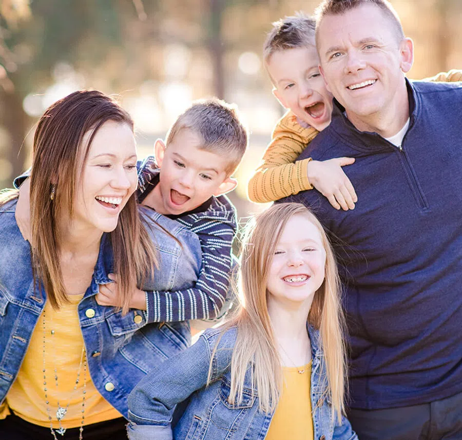 Happy family outdoors smiling, parents with three kids wearing casual colorful clothes on a sunny day.