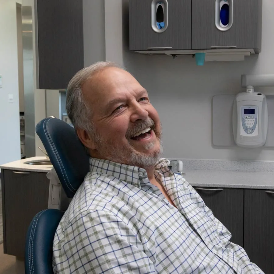 Smiling senior man sitting in dental chair in modern clinic wearing a checkered shirt
