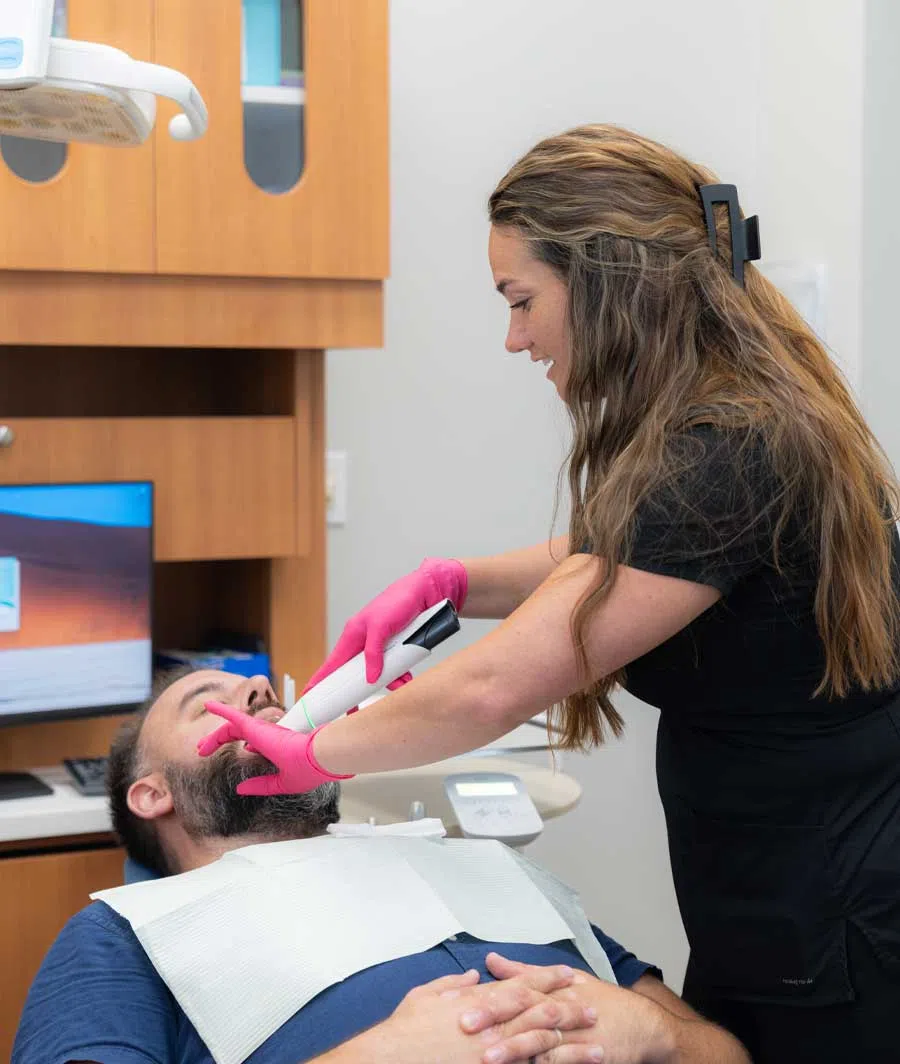 Dental hygienist in pink gloves using a device inside a male patient's mouth during a dental checkup.