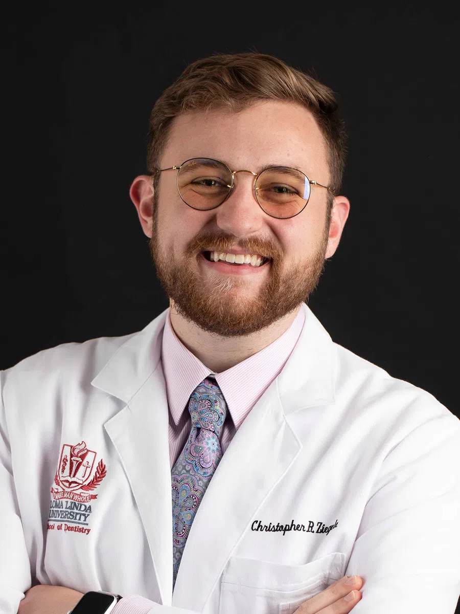 Smiling male dentist wearing glasses and a white lab coat with Loma Linda University School of Dentistry logo