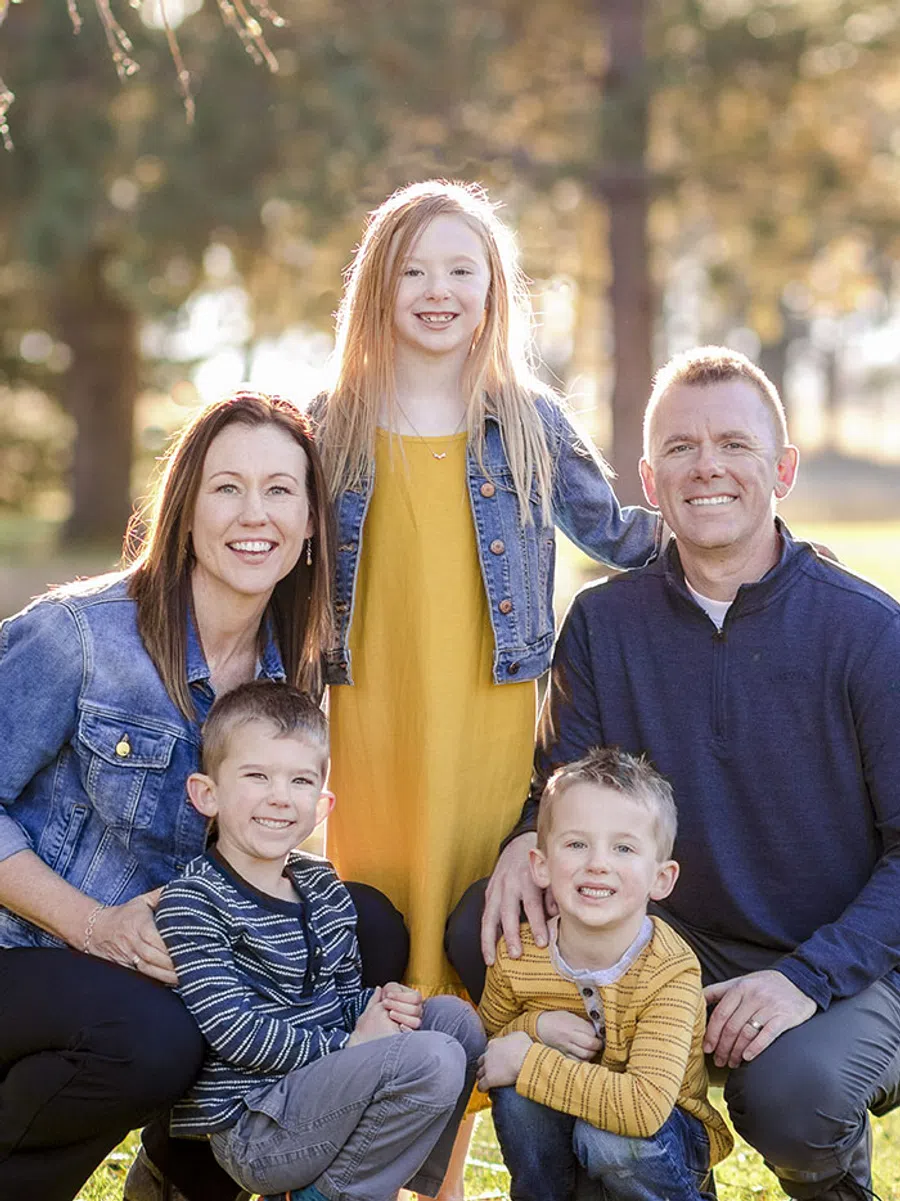 Smiling family of five outdoors with parents and three children in casual autumn clothing during sunset.