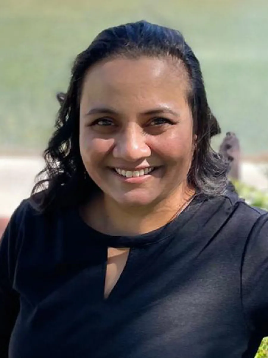Smiling woman with wavy dark hair wearing a black top outdoors in bright sunlight