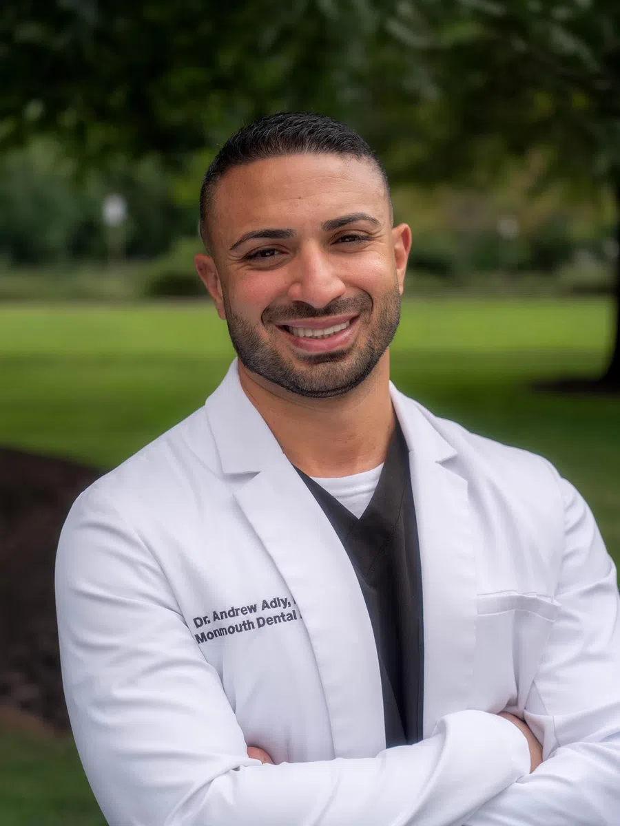 Smiling male healthcare professional wearing a white coat and black scrubs in an office setting