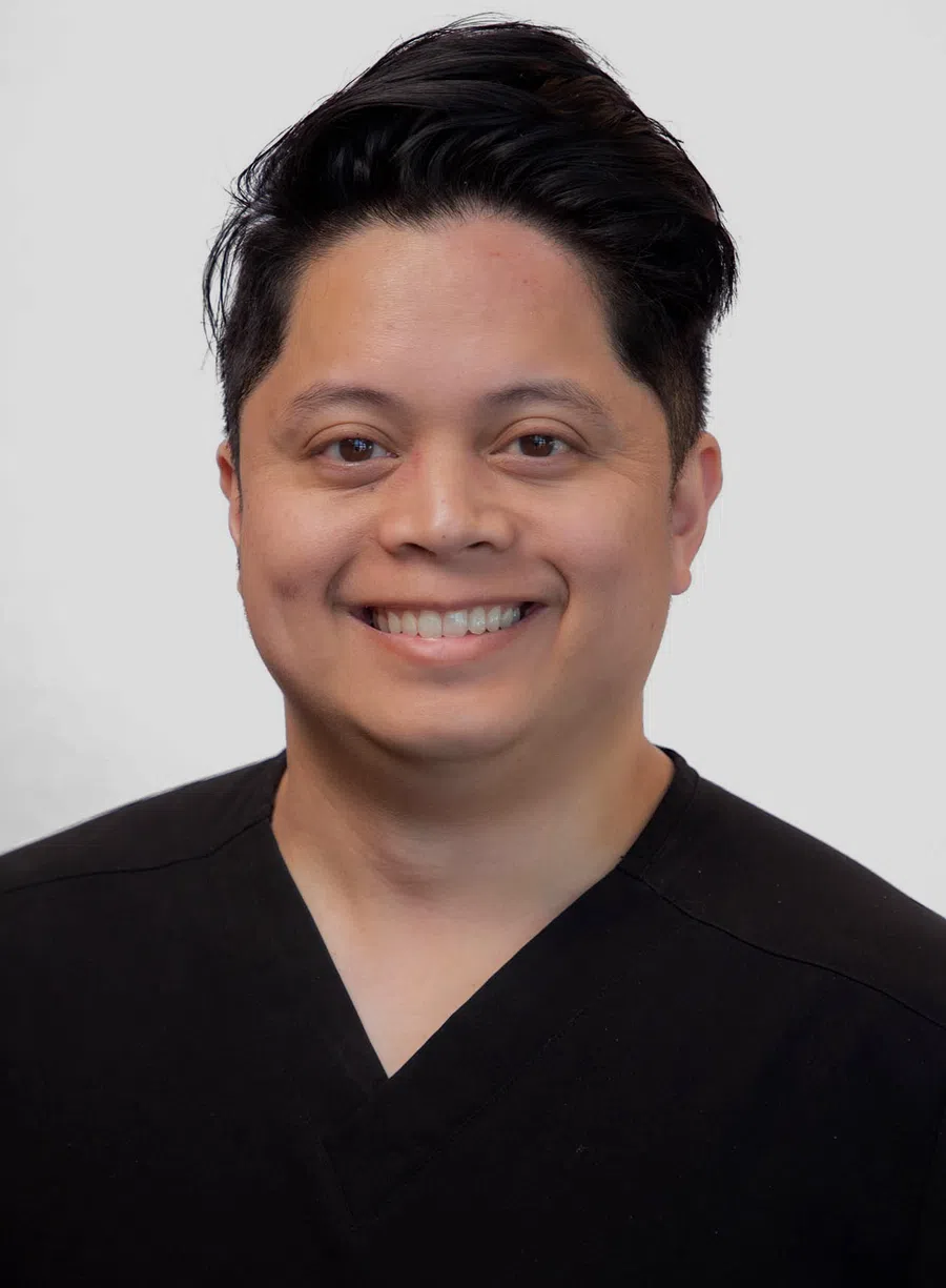 Smiling man with short black hair wearing a black V-neck shirt against a plain white background.