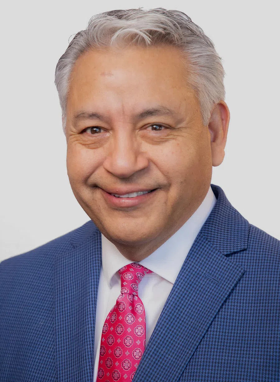 Smiling middle-aged man with gray hair wearing a blue suit and pink patterned tie on white background