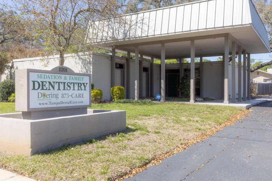 Dental office building with signage for sedation and family dentistry and contact information in sunny setting.