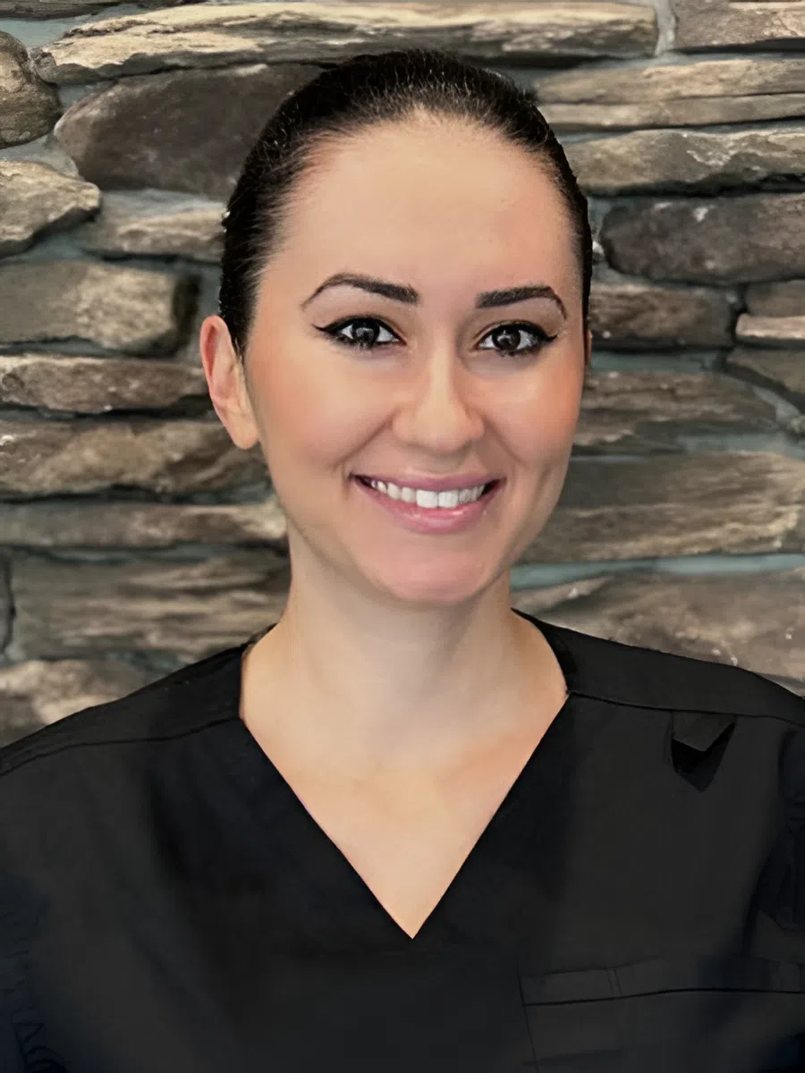 Smiling woman with dark hair wearing black uniform standing in front of stone wall background