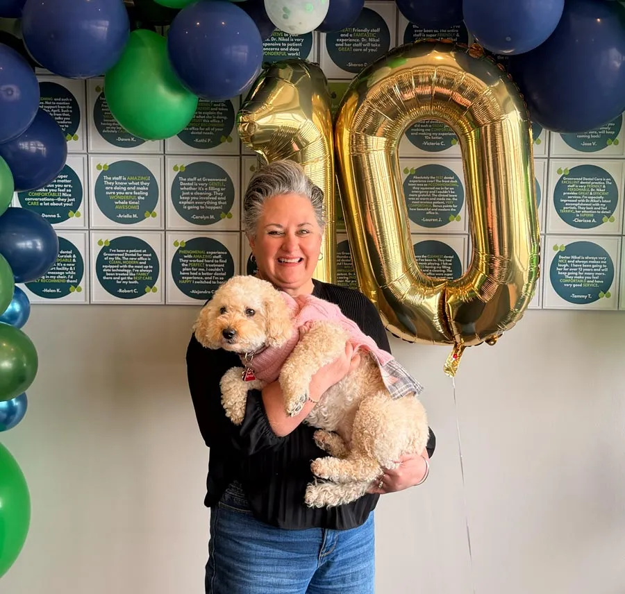 Woman smiling and holding a small dog in front of blue and green balloons and a gold number 10 balloon
