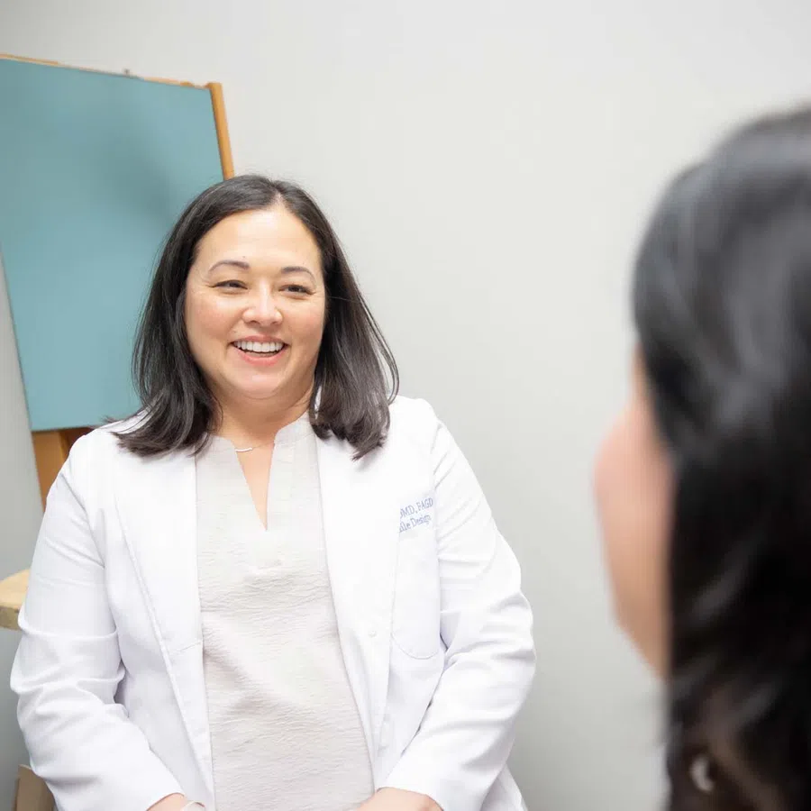 Female doctor smiling and talking to a patient in a medical office setting.