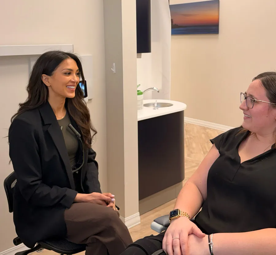 Two women sitting and smiling in a modern office or clinic setting during a conversation.