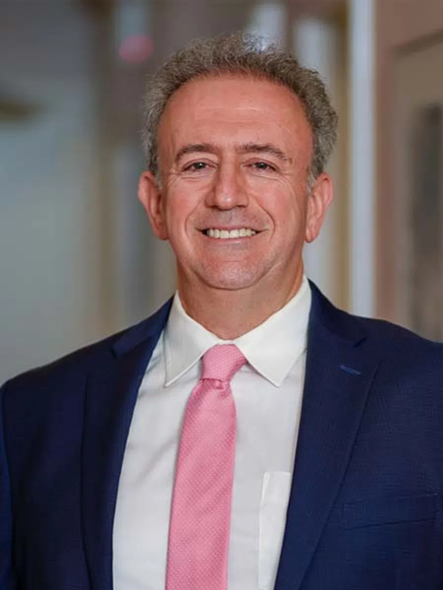Smiling middle-aged man with gray hair wearing black medical scrubs with NYNJOS logo outdoors.