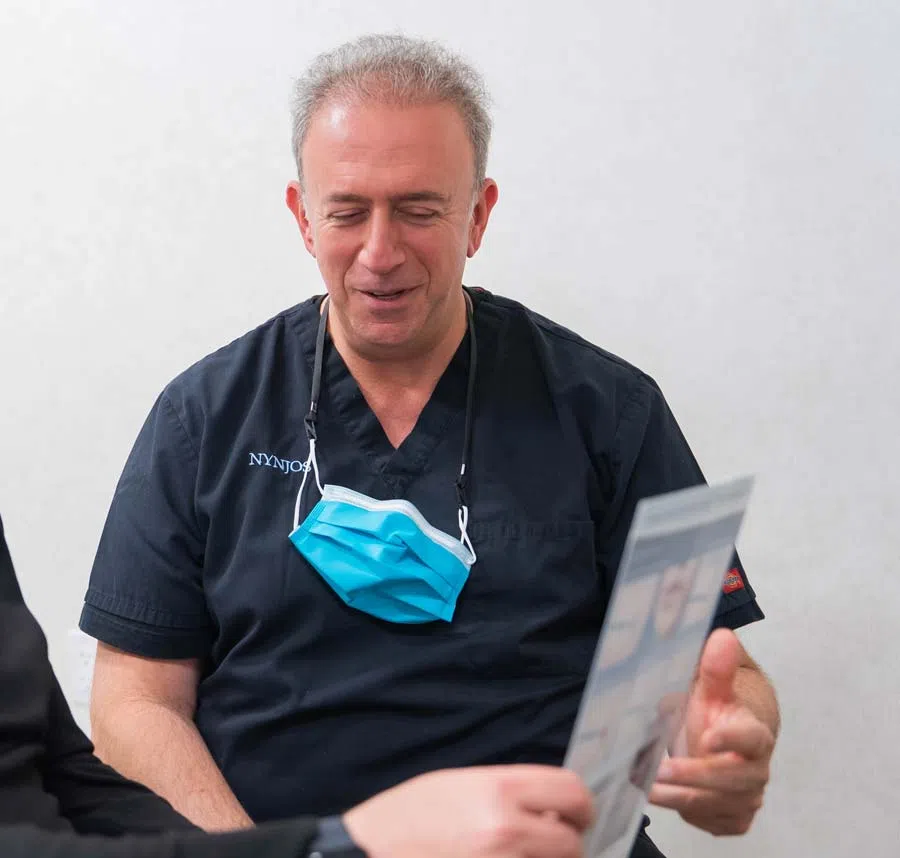 Male healthcare professional in black scrubs with face mask hanging discusses medical images with patient.