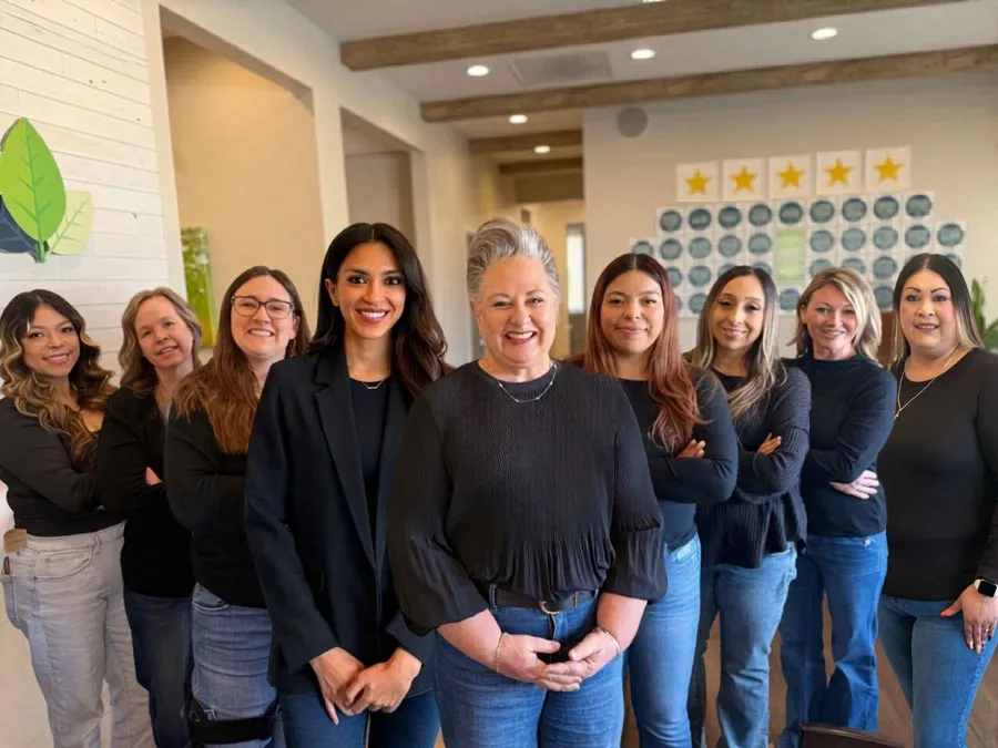 Diverse group of nine professional women standing in an office hallway smiling and posing confidently.
