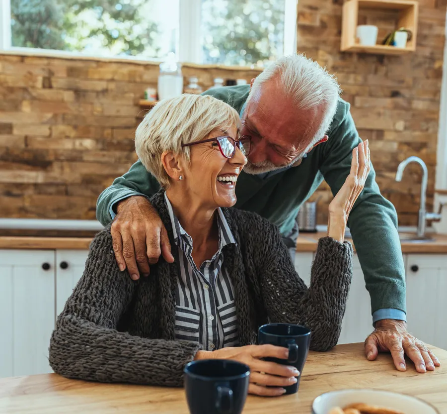 Happy elderly couple sharing a joyful moment in a cozy kitchen with coffee mugs on the wooden table